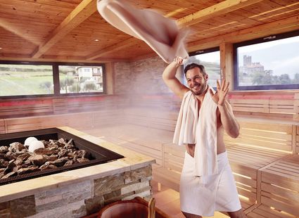 Ein Mann schwingt im Sauna Tower im Preidlhof ein Handtuch neben dem Aufgussofen.