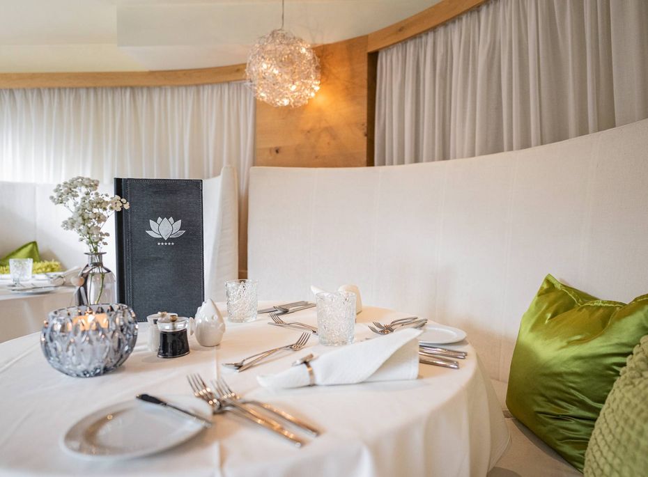 Gourmetrestaurant mit gedecktem Tisch im Preidlhof Ein elegant gedeckter Tisch mit weißen Stühlen und grünen Kissen im Gourmetrestaurant.