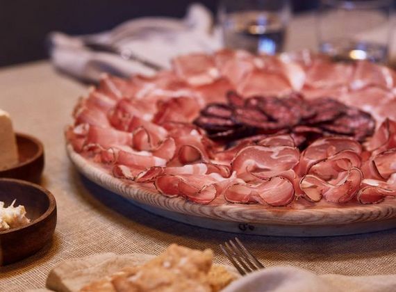 Un grande piatto di salumi sottili è disposto su un tavolo accanto a piccole ciotole e forchette.