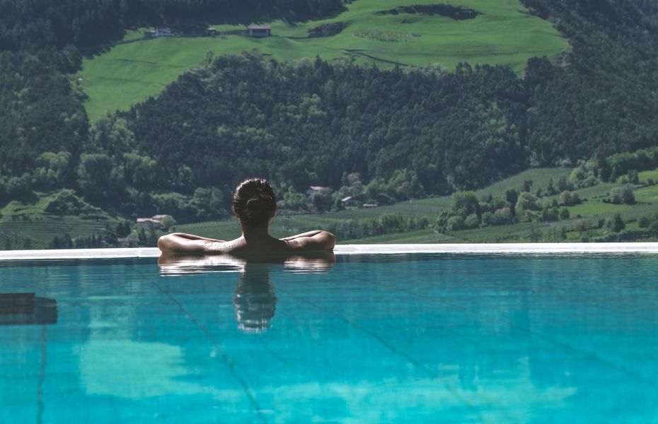 Infinity-Pool mit Bergblick im Preidlhof Eine Person lehnt im Infinity-Pool und blickt auf die grünen Berge im Hintergrund.
