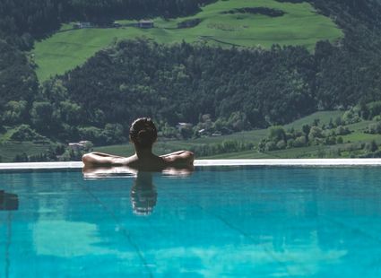 Eine Person lehnt im Infinity-Pool und blickt auf die grünen Berge im Hintergrund.
