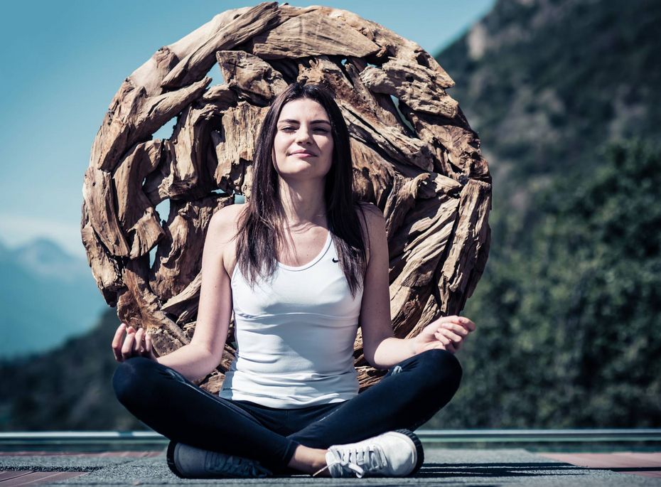 Meditation auf der Terrasse im Preidlhof Eine Frau sitzt auf der Terrasse im Schneidersitz und meditiert vor einer großen Holzskulptur.