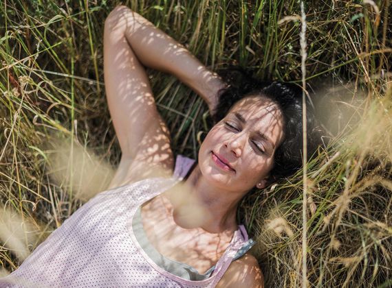 Eine Frau liegt entspannt im Gras und schließt die Augen.