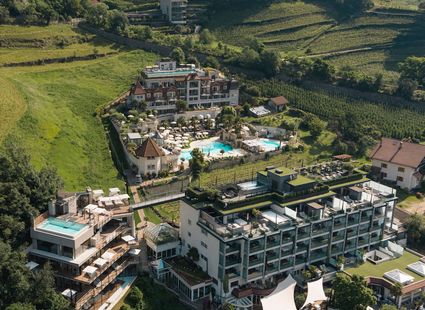 Eine weitläufige Hotelanlage mit Pools und Terrassen liegt zwischen grünen Hängen in Naturns.