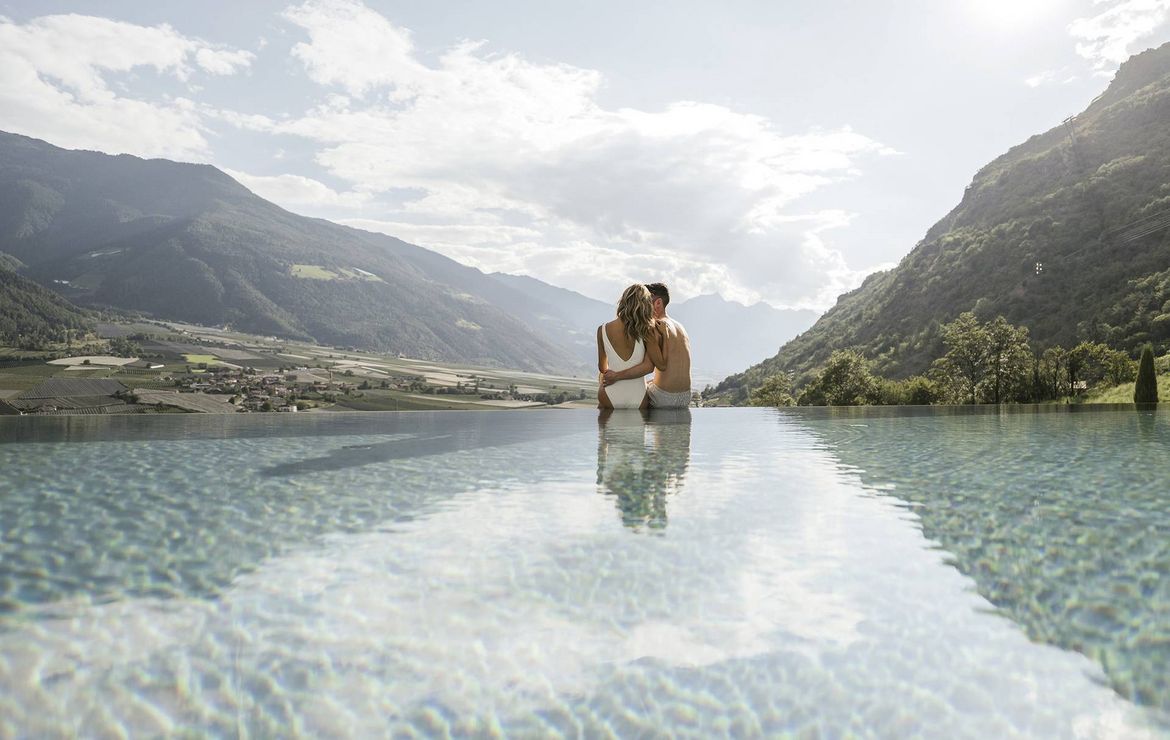 Ein Paar steht eng umschlungen im Infinity-Pool mit Blick auf die Berge.