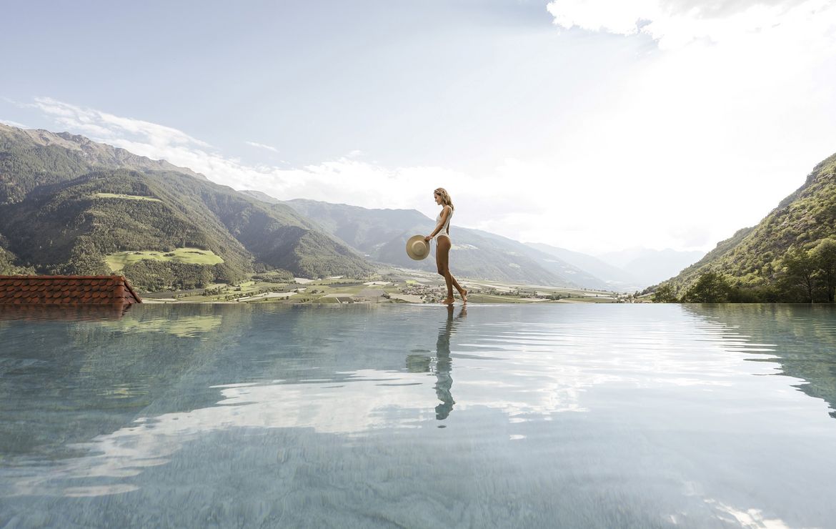 A woman stands at the edge of an infinity pool overlooking a mountain valley.