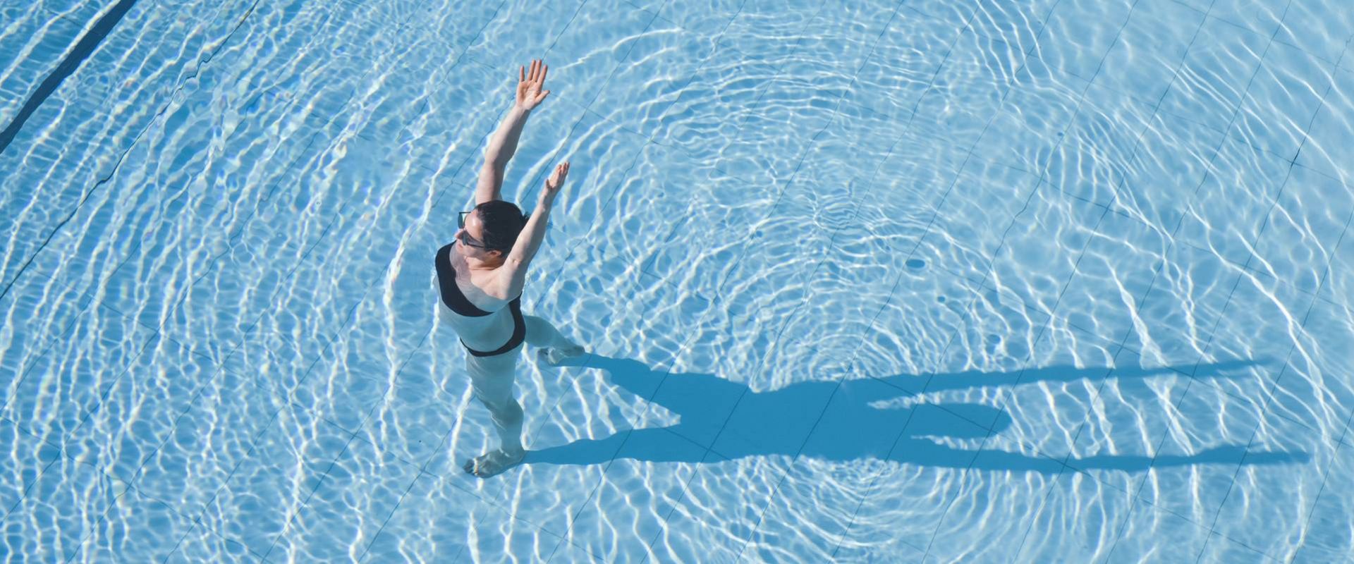 A swimmer is seen from above in a clear blue infinity pool, with ripples spreading across the water.