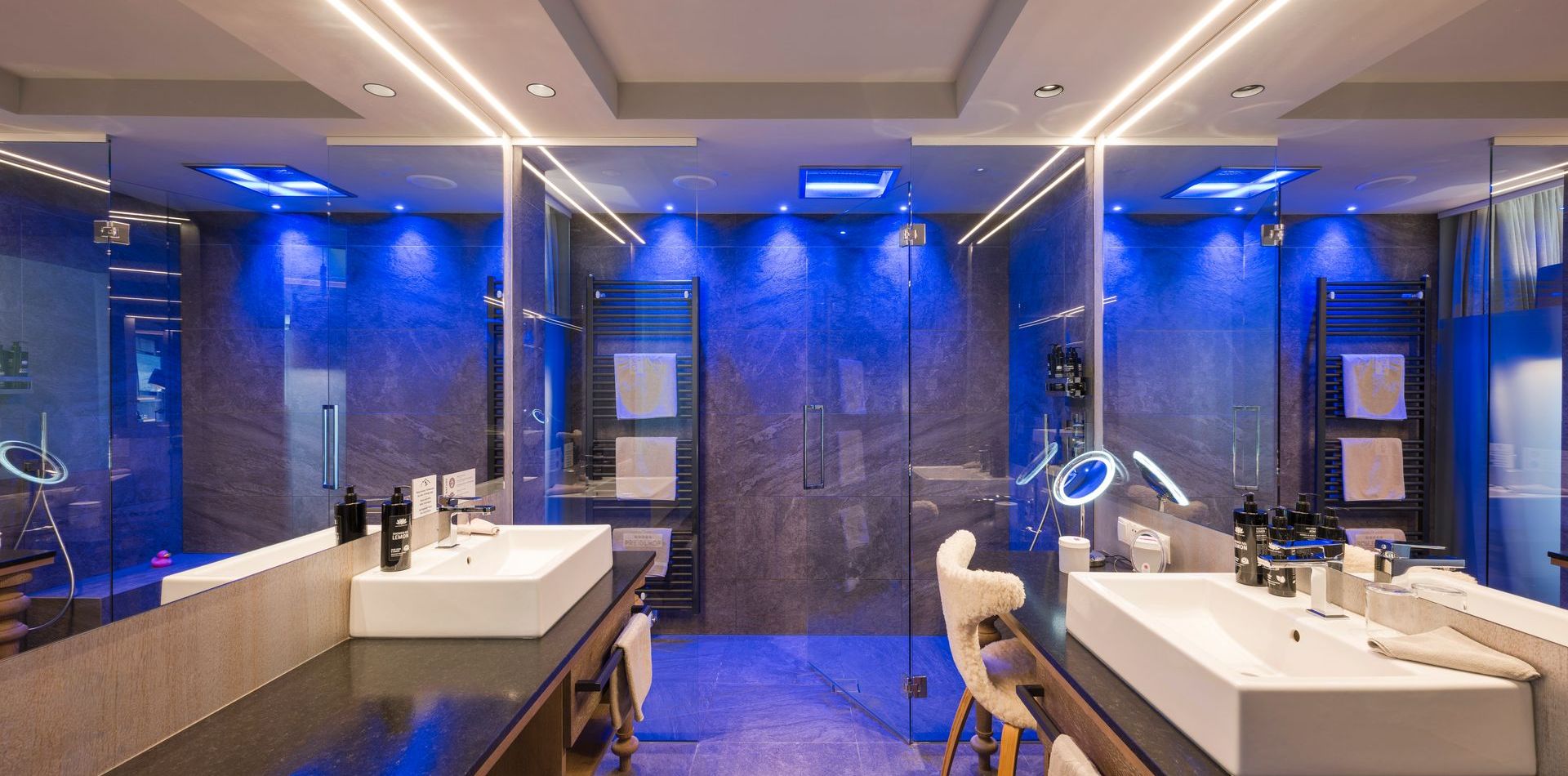 Ein modernes Badezimmer mit zwei Waschtischen, großflächigen Spiegeln und blauer Beleuchtung im Comfort Room Pink.