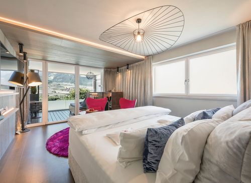 Ein modernes Hotelzimmer mit Doppelbett, pinken Akzenten, Balkon und Blick in die Berge.