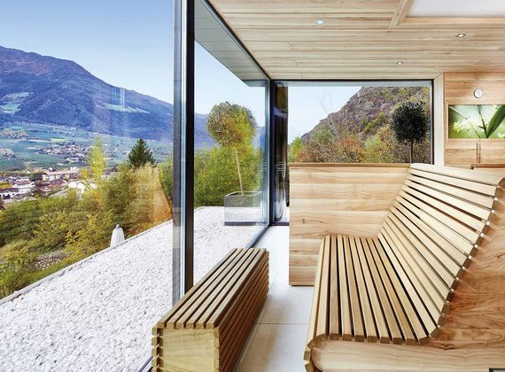Eine Holzsauna mit großer Glasfront und Blick auf die Berge und das Tal.