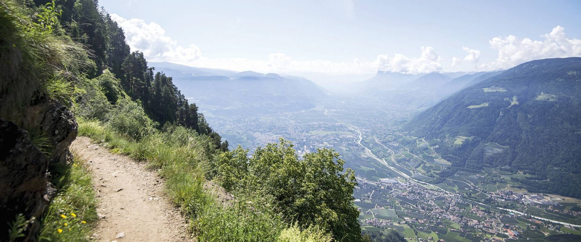 Ein schmaler Wanderweg verläuft am steilen Hang mit weitem Blick über das Tal und die Berge.