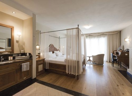 A luxury suite bedroom with a four-poster bed, vanity area, desk and sitting space by the window.