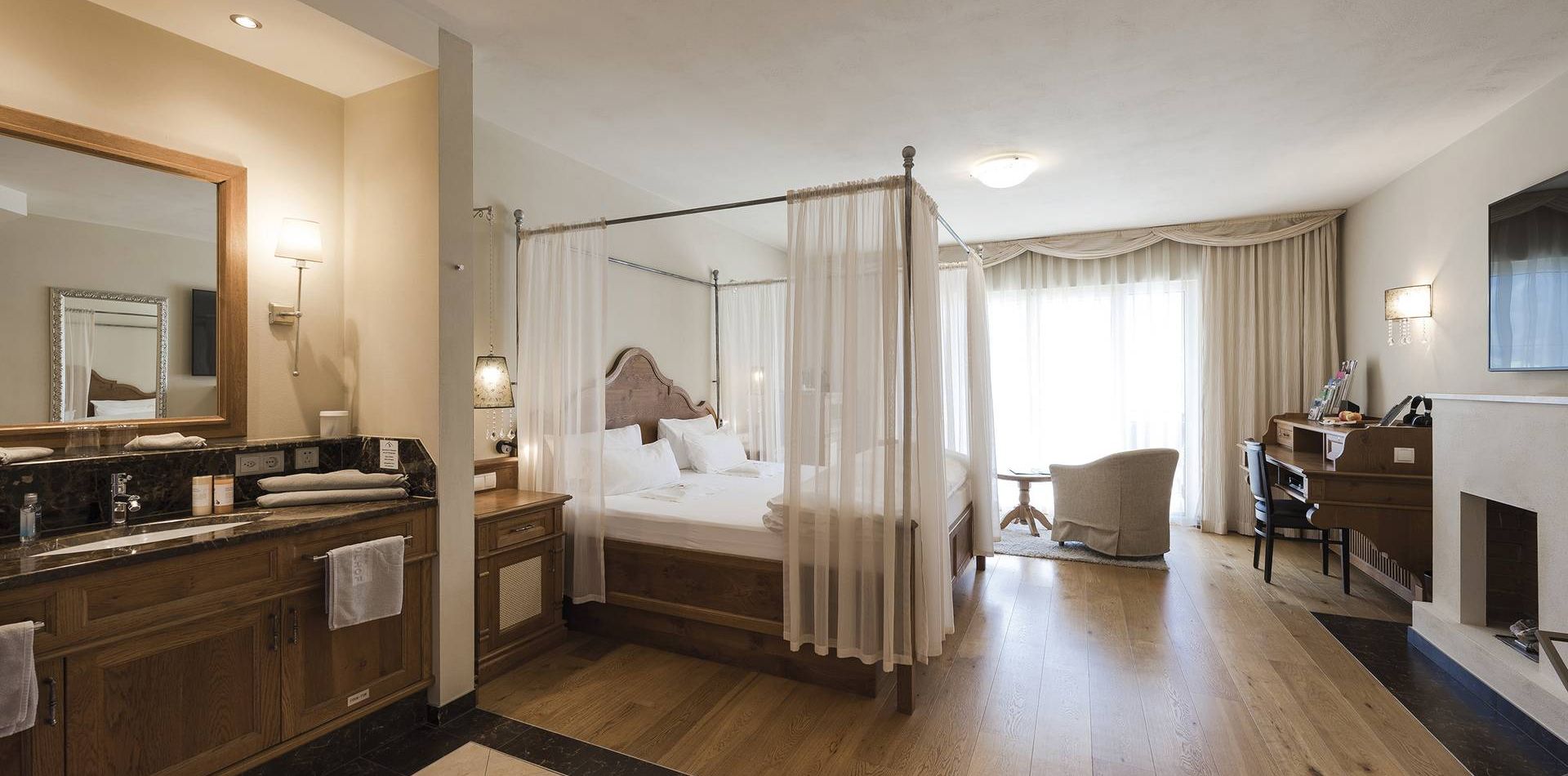 Una camera suite di lusso con letto a baldacchino, zona vanity, scrivania e salotto vicino alla finestra.