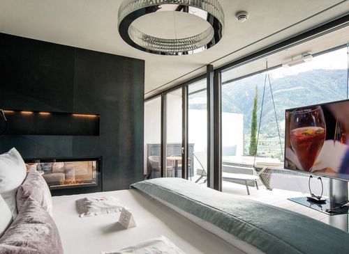 Penthouse Suite DolceVita with mountain-view terrace A modern penthouse suite with a large bed, floor-to-ceiling windows, TV and terrace facing the mountains.