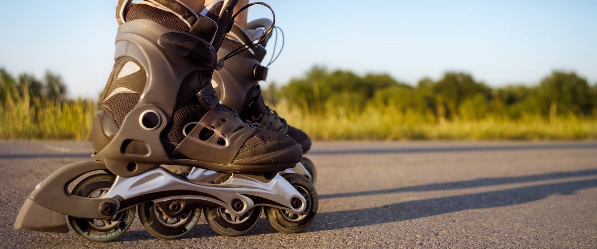 Eine Person steht mit Inlineskates auf einer asphaltierten Straße im Freien, im Hintergrund Grün und warmes Licht.