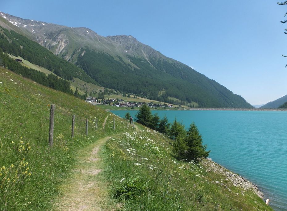 Wanderweg am See im Südtiroler Bergland Ein schmaler Wanderweg verläuft entlang eines türkisfarbenen Sees vor grünen Hängen und hohen Bergen.