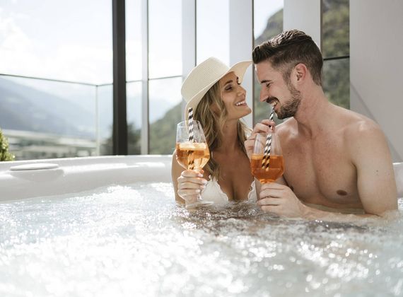 Ein Paar sitzt im Whirlpool und hält im Adults Only Wellnesshotel zwei Getränke in der Hand.
