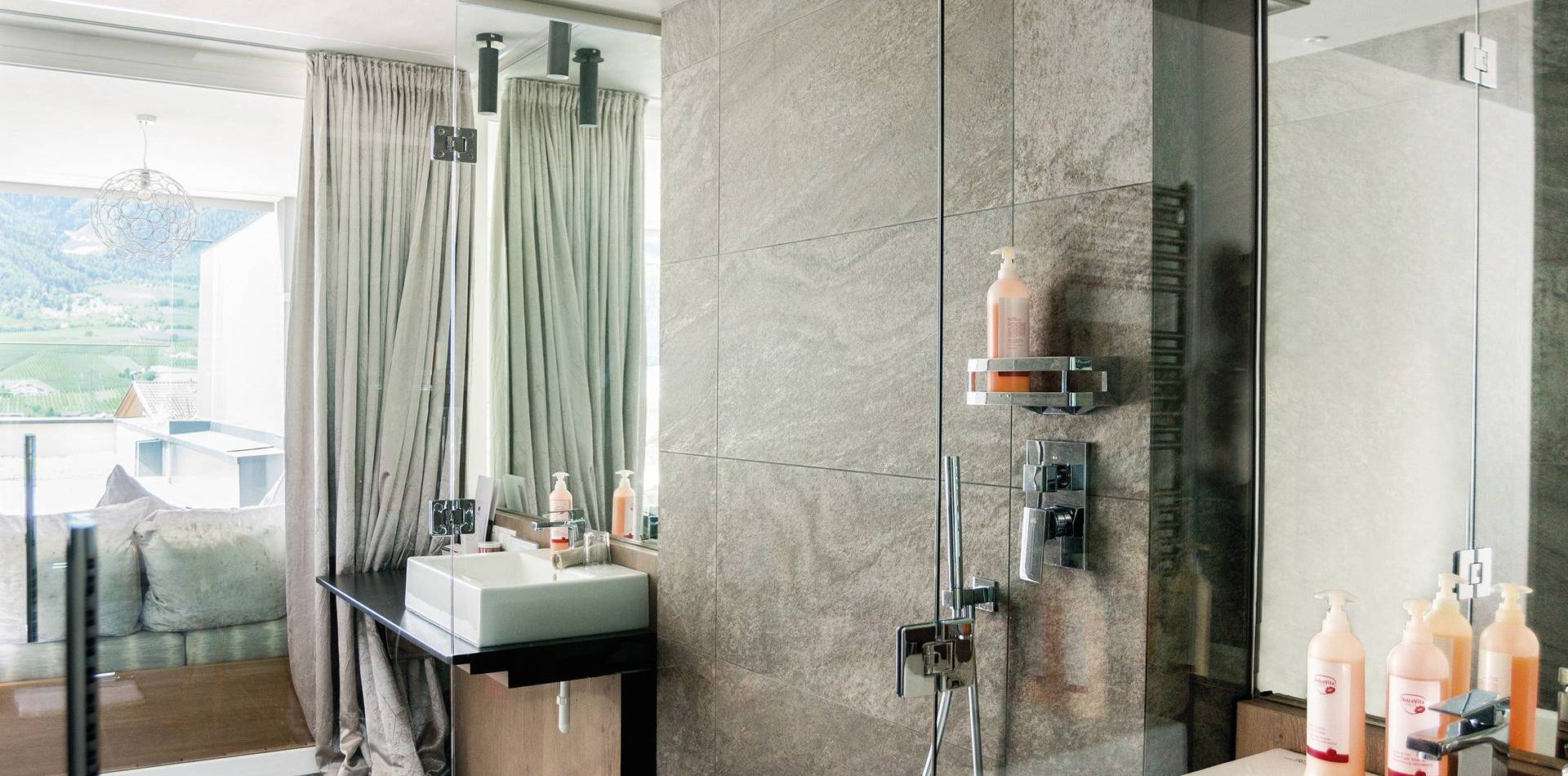 Un bagno suite moderno con doccia in vetro, lavabo e vista sulla camera e sulle montagne.