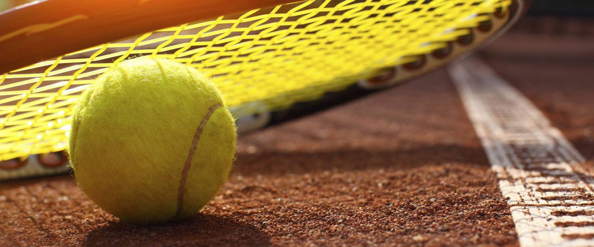Ein Tennisball liegt auf einem Tennisschläger auf dem roten Sandplatz.