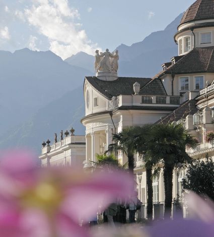 Der Preidlhof mit Palmengarten und Bergpanorama ist hinter unscharfen Blumen im Vordergrund zu sehen.