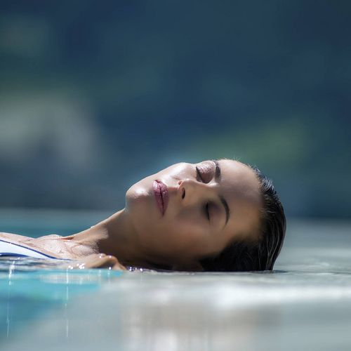 Eine Frau entspannt im Infinity-Pool und treibt mit geschlossenen Augen auf dem Wasser.