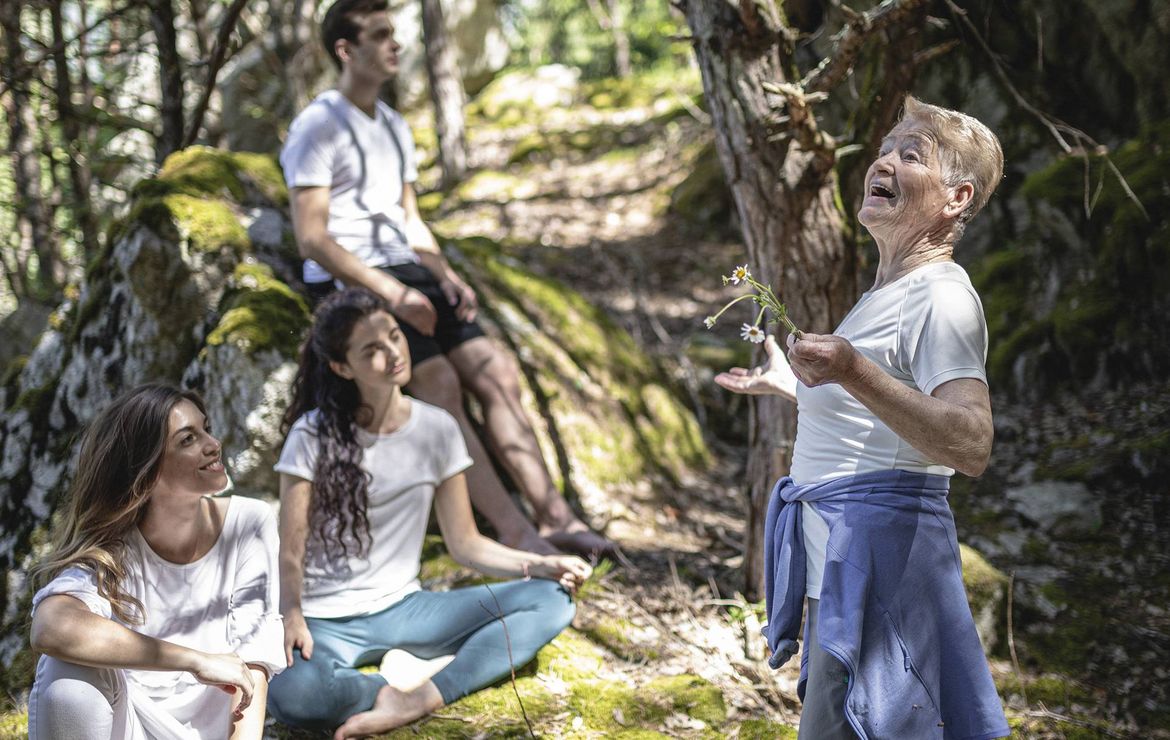 Eine Trainerin leitet eine Retreat-Class im Wald, während drei Teilnehmende auf dem Boden sitzen und zuhören.