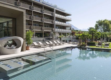 Der Außenpool mit Liegen und Lounge-Bereich liegt vor dem modernen Hotelgebäude.