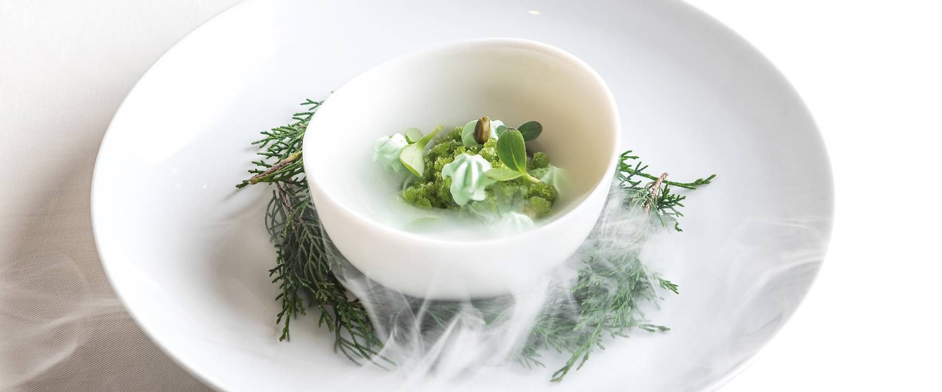Una piccola ciotola con antipasto gourmet è servita su un piatto bianco con erbe aromatiche attorno.