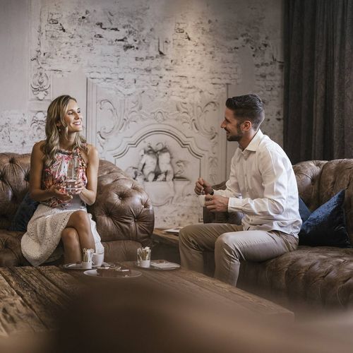 Zwei Gäste sitzen auf einer Chesterfield-Sitzgruppe in einer stilvollen Lounge und unterhalten sich.
