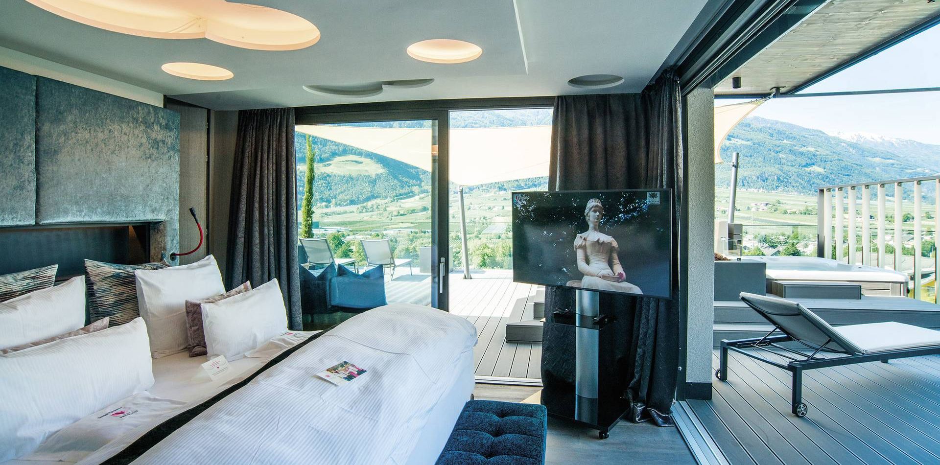 Una penthouse suite con letto grande, porte scorrevoli in vetro e terrazza affacciata sulle montagne.
