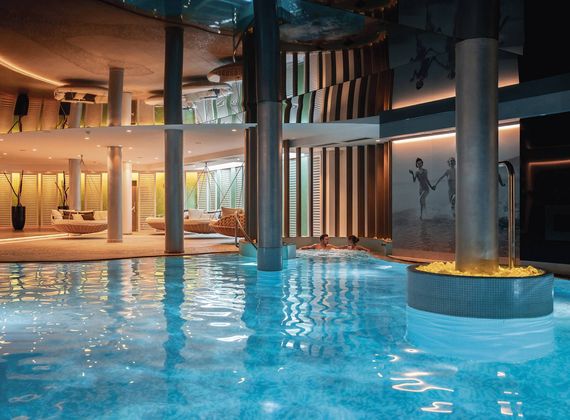Ein Innenpool mit ruhigem Wasser, Liegen und warm beleuchteten Ruhebereichen im Spa.