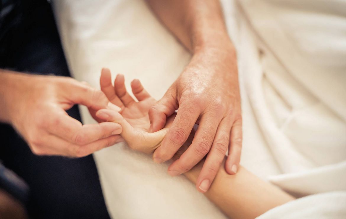 Hands gently massage a guest’s forearm during a wellness treatment.