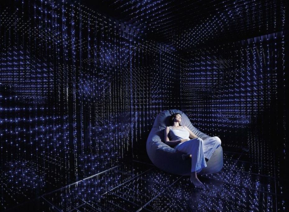 Ruheraum mit Lichtinstallation im Preidlhof Eine Frau sitzt entspannt in einem gepolsterten Sessel in einem dunklen Ruheraum mit blau-violetter Lichtinstallation.
