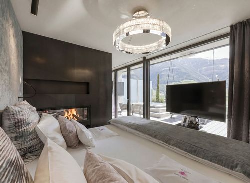 Die Penthouse Suite zeigt ein Bett, einen Kamin, einen Fernseher und bodentiefe Fenster mit Blick auf die Berge.