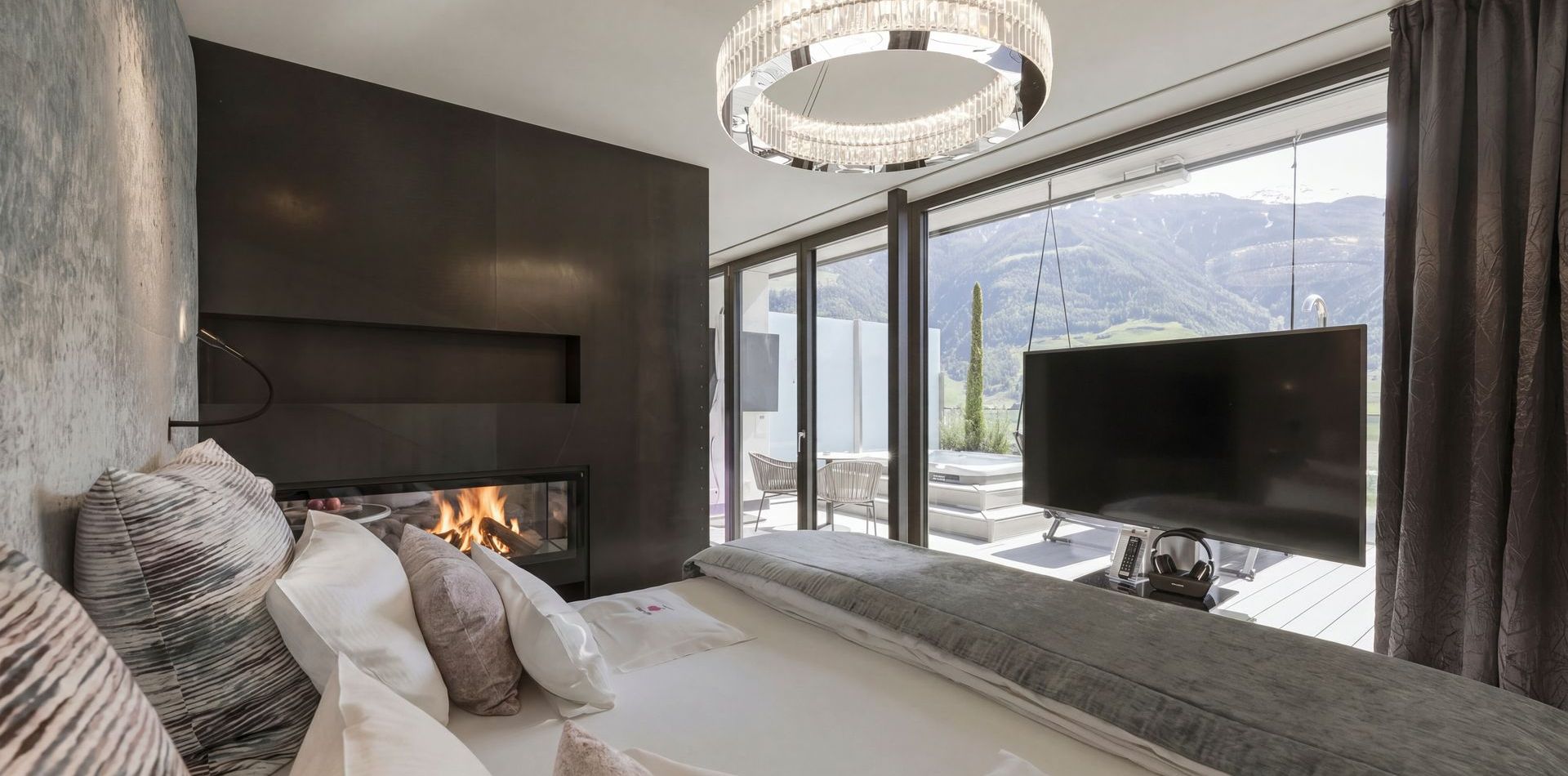 Die Penthouse Suite zeigt ein Bett, einen Kamin, einen Fernseher und bodentiefe Fenster mit Blick auf die Berge.