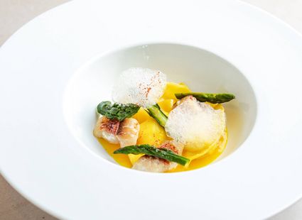 Eine weiße Schale mit Spargel, Gemüse und feiner Sauce in einer eleganten Gourmetküche-Anrichtung.