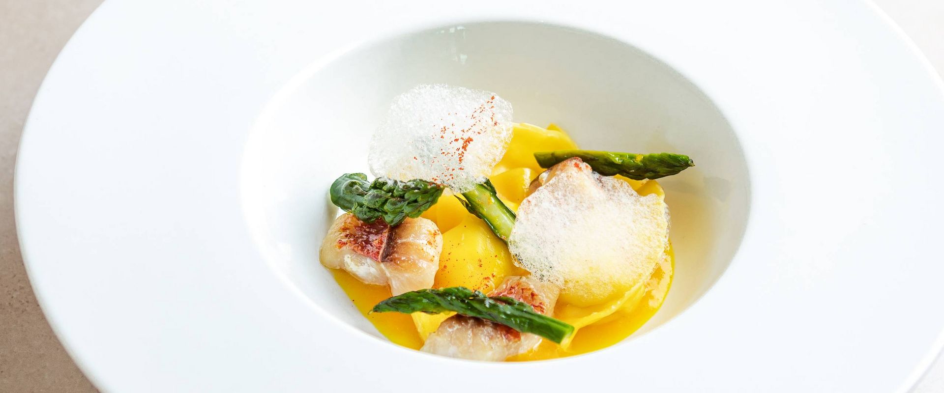 Eine weiße Schale mit Spargel, Gemüse und feiner Sauce in einer eleganten Gourmetküche-Anrichtung.
