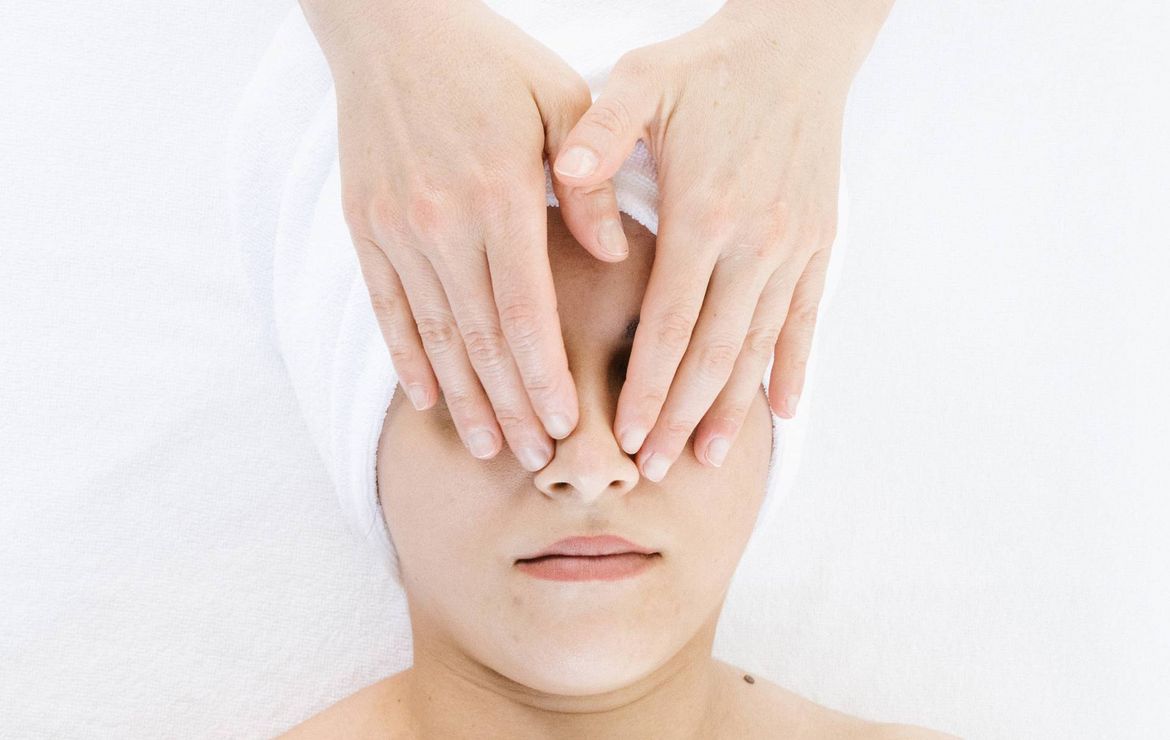 Hands gently cover a woman's eyes during a facial spa treatment on a white treatment bed.