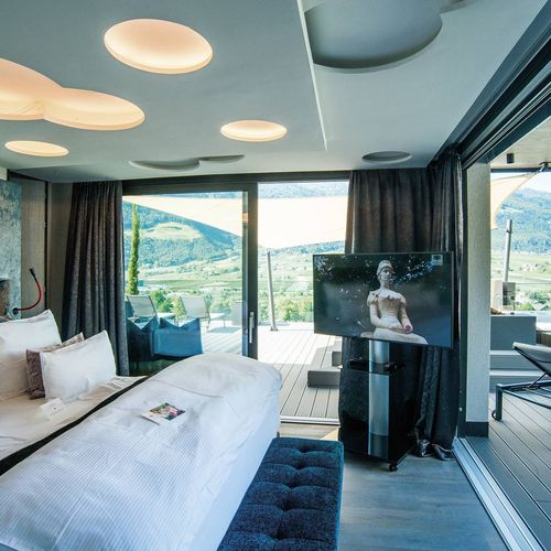 Eine moderne Suite mit Doppelbett, TV und Terrasse mit Liegen und Bergblick im Wellnesshotel.