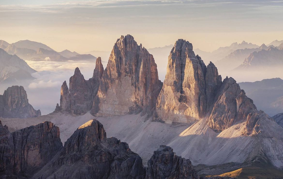 Berggipfel der Dolomiten ragen im warmen Morgenlicht über ein Meer aus Nebel.