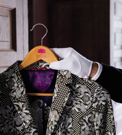 Eine gloved Hand hält ein gemustertes Sakko auf einem Preidlhof-Kleiderbügel vor einer Tür.