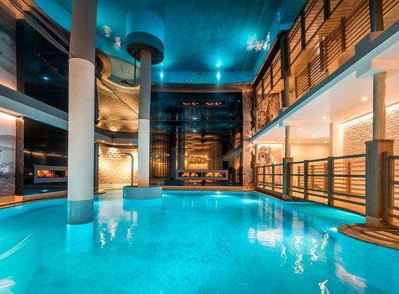 Ein beleuchteter Indoor-Pool mit türkisfarbenem Wasser in einem modernen Wellnessbereich.