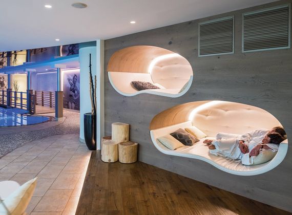 Ein moderner Wellnessbereich mit organisch geformten Schlafnischen und Liegen neben einem Pool.