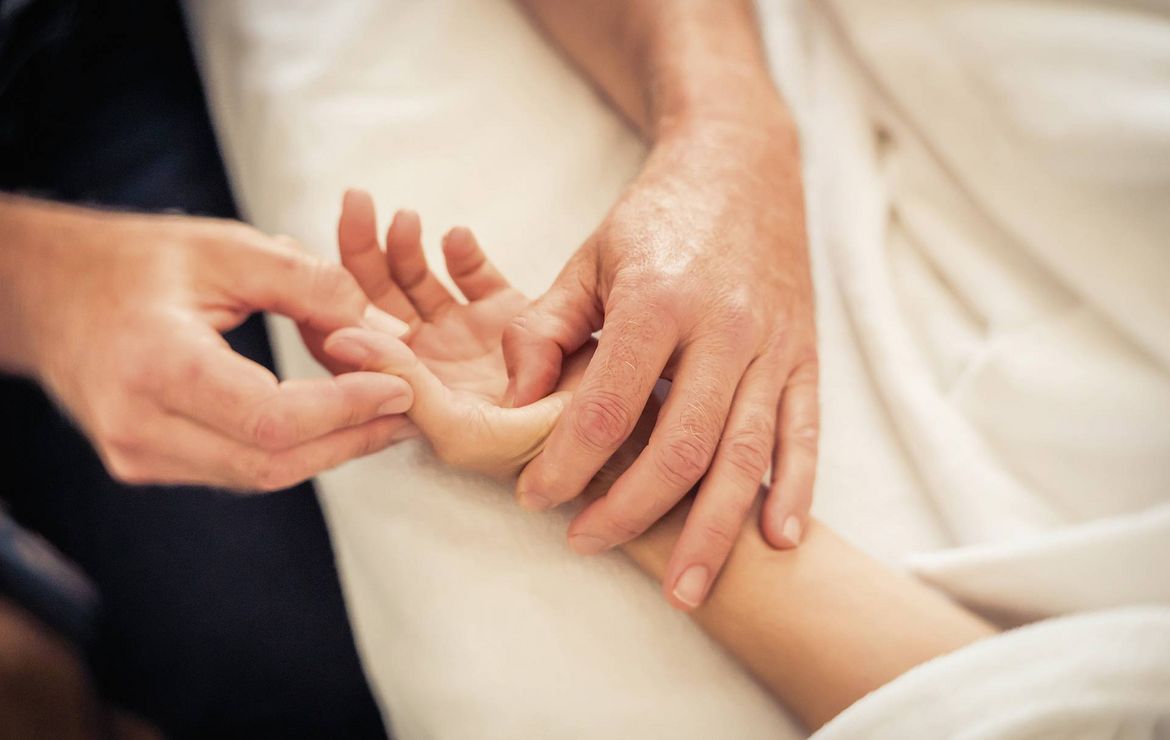 Sanfte Hände massieren den Arm einer schwangeren Person während einer Wellnessbehandlung.