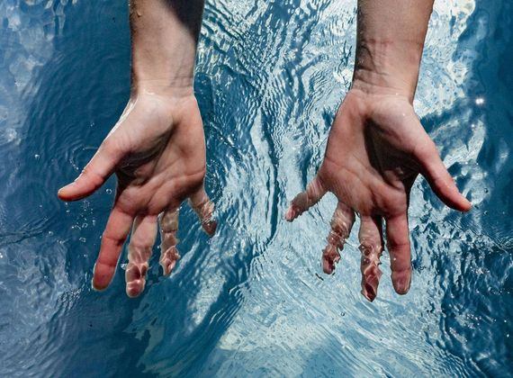 Two hands move through the rippling surface of a thermal water pool.
