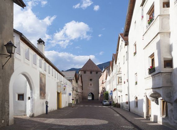 Eine historische Gasse mit weiß verputzten Häusern führt auf ein altes Stadttor zu.