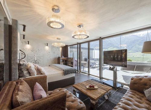 Ein modernes Schlafzimmer der Penthouse Suite mit Sofa, Holztisch und großer Glasfront zum Balkon mit Bergblick.