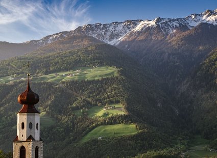 Ein Kirchturm mit einer traumhaften Bergkulisse im Hintergrund.
