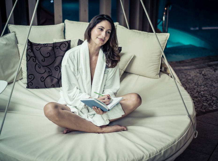 Entspannungsliege im Wellnesshotel in Naturns Eine Frau sitzt im Bademantel auf einer runden Entspannungsliege und hält ein Notizbuch in den Händen.