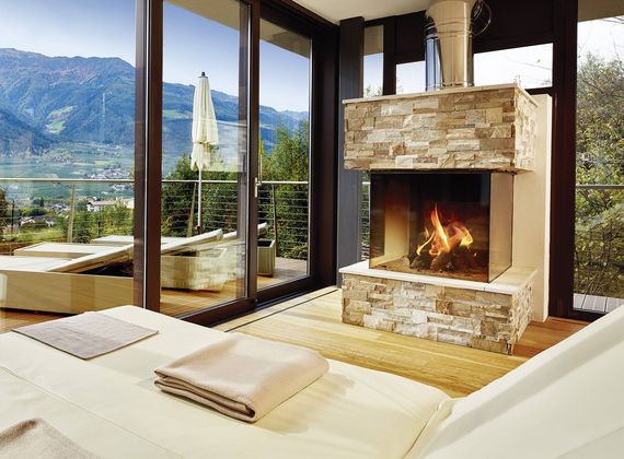 A sauna lounge with a stone fireplace, lounge beds and large windows overlooking the mountains.